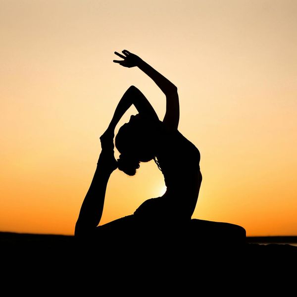 Silhouette of a person in a strong warrior yoga pose at sunset.